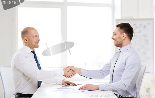 Image of two smiling businessmen shaking hands in office