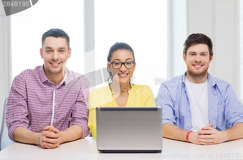 Image of three smiling colleagues with laptop in office