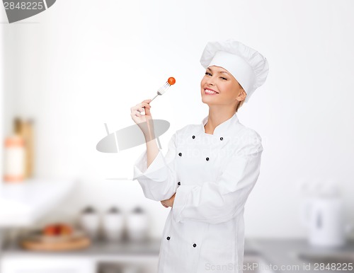 Image of smiling female chef with fork and tomato