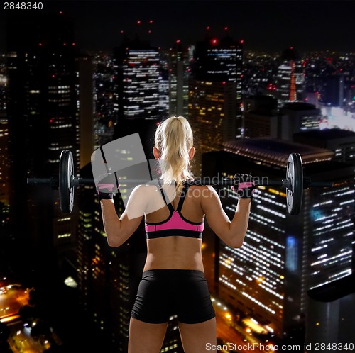 Image of sporty woman exercising with barbell from back