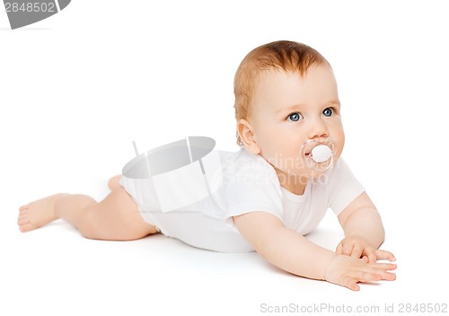 Image of smiling baby lying on floor with dummy in mouth