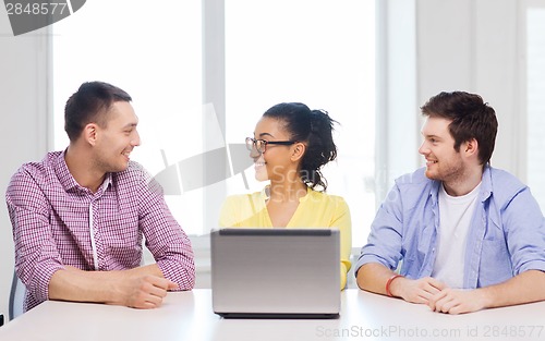 Image of three smiling colleagues with laptop in office