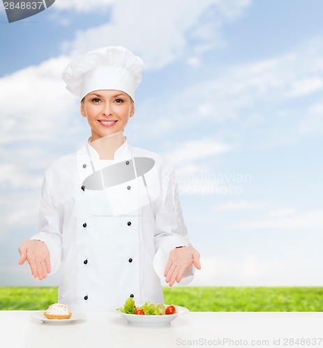 Image of smiling female chef with salad and cake on plates