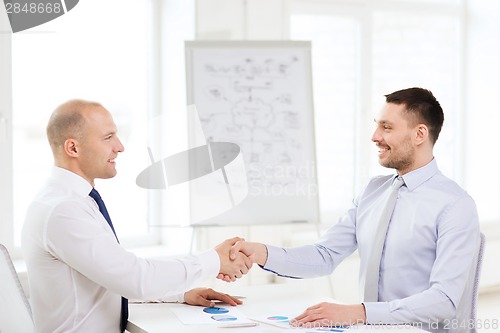 Image of two smiling businessmen shaking hands in office