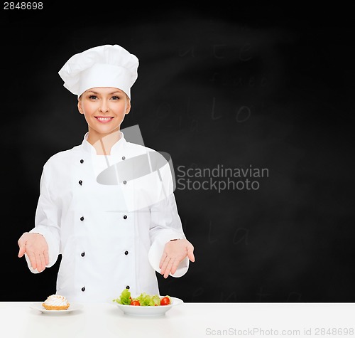 Image of smiling female chef with salad and cake on plates