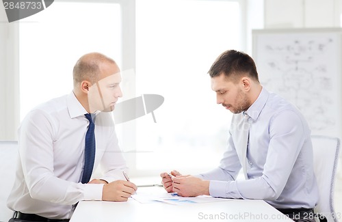 Image of two serious businessman with papers in office