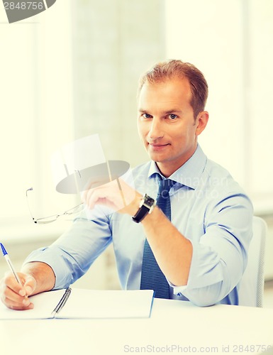 Image of businessman with spectacles writing in notebook