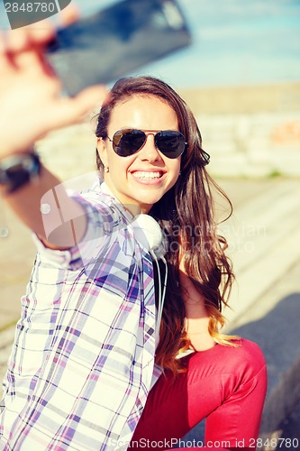 Image of smiling teenager taking picture with smartphone