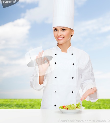 Image of smiling female chef with salad on plate