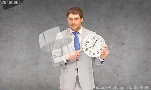 Image of handsome businessman pointing finger to wall clock
