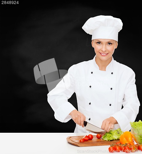 Image of smiling female chef chopping vegetables