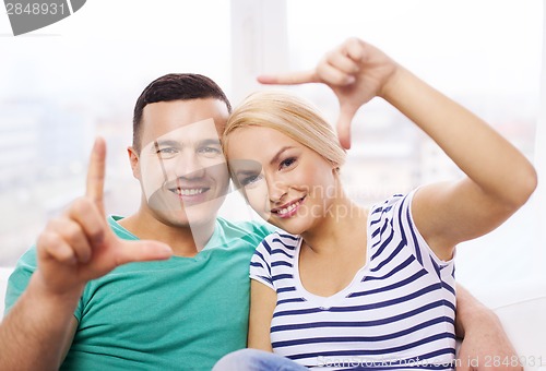 Image of smiling happy couple making frame gesture at home