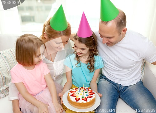 Image of smiling family with two kids in hats with cake