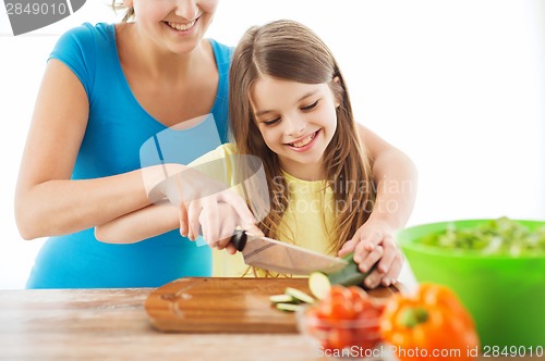 Image of smiling little girl with mother chopping cucumber
