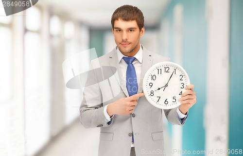 Image of handsome businessman pointing finger to wall clock