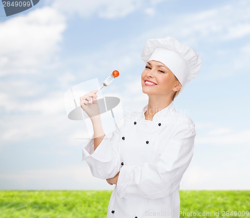 Image of smiling female chef with fork and tomato