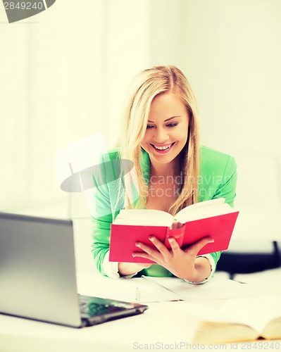Image of smiling student girl reading book in college