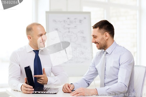 Image of two smiling businessmen with laptop in office