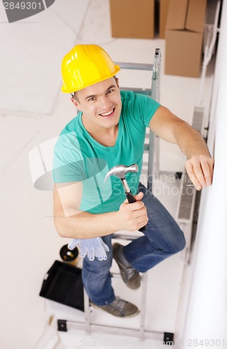 Image of smiling man in helmet hammering nail in wall