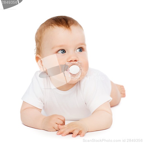 Image of smiling baby lying on floor with dummy in mouth