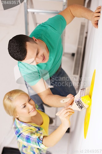 Image of smiling couple painting wall at home