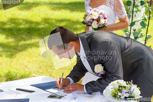 Image of groom signing certificate in park 