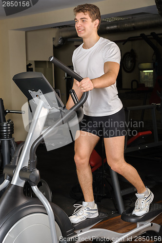 Image of young man does workout at elliptical trainer in gym