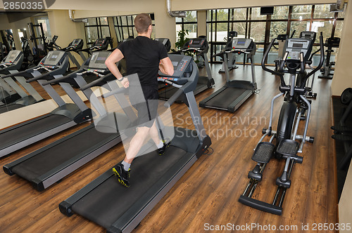 Image of young man running at treadmill in gym