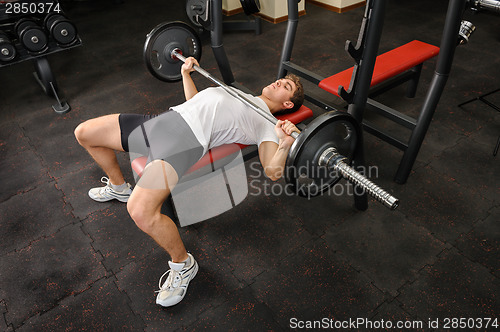 Image of young man doing bench press workout in gym