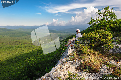 Image of Hiking man in rays of sunset sitting at the edge