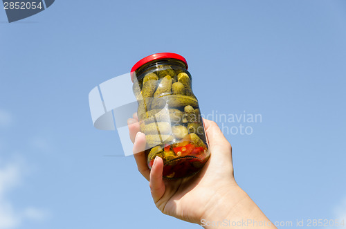 Image of cucumber jar in female hand on blue sky background 