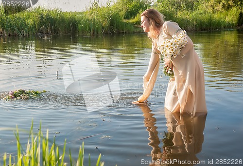 Image of Attractive woman lowers wreath in water