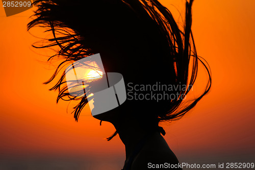 Image of Silhouette of woman tossing hair at sunset