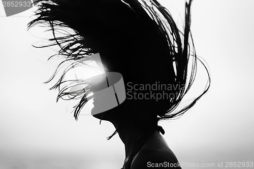 Image of Silhouette of woman tossing hair at sunset black and white