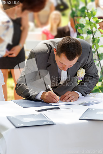 Image of groom signing certificate in park 