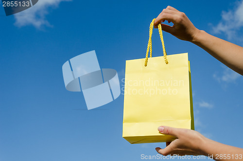 Image of hand hold yellow paper bag on blue sky background 