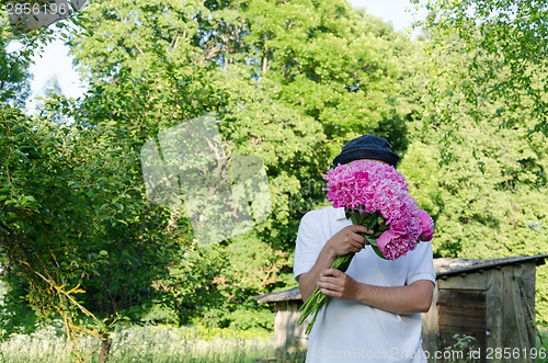 Image of man hiding his face with peony bouquet garden  