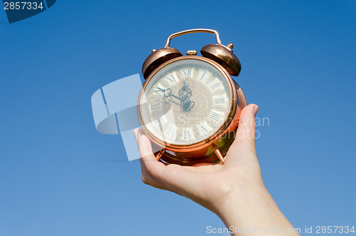 Image of clock roman numeral in hand on blue sky background 