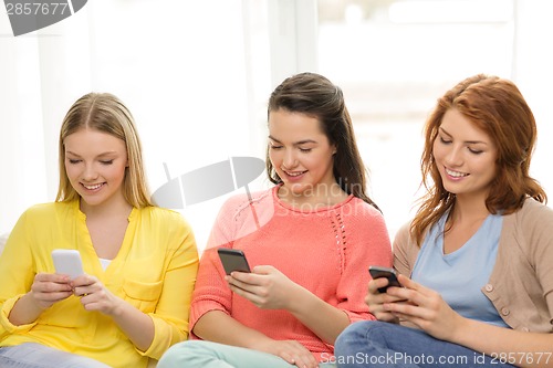 Image of smiling teenage girls with smartphones at home