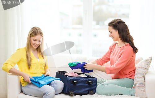 Image of two smiling teenage girls packing suitcase at home