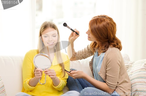 Image of two smiling teenage girls applying make up at home