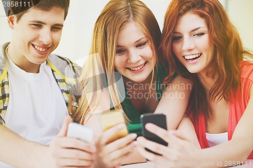 Image of three smiling students with smartphone at school