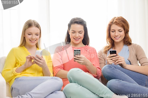 Image of smiling teenage girls with smartphones at home