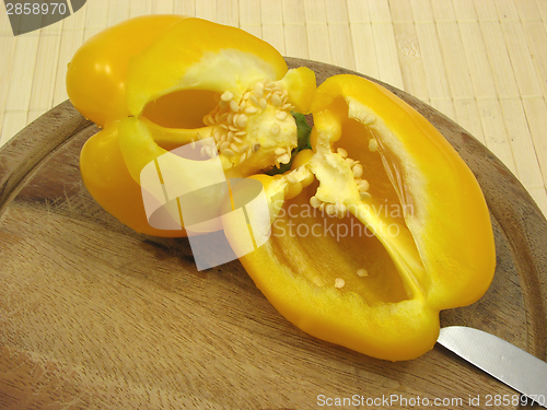 Image of Halved yellow pepper on wooden plate  with knife