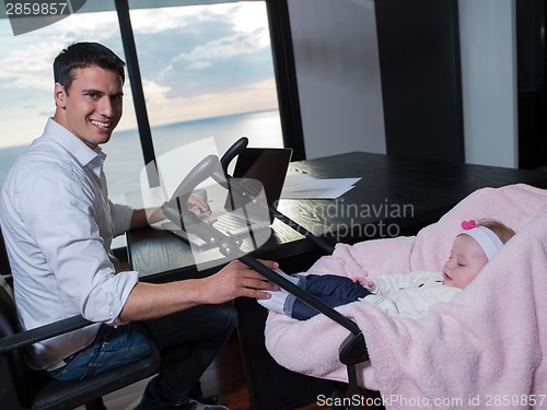 Image of man working from home and take care of baby