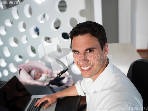 Image of man working from home and take care of baby