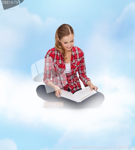 Image of smiling young woman sitting on floor with book
