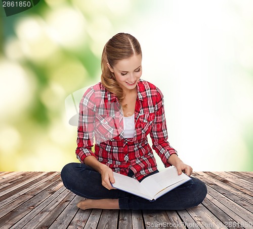 Image of smiling young woman sitting on floor with book