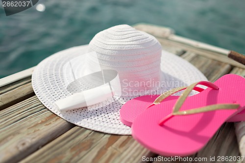 Image of close up of hat, sunscreen and slippers at seaside