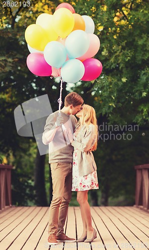 Image of couple with colorful balloons kissing in the park